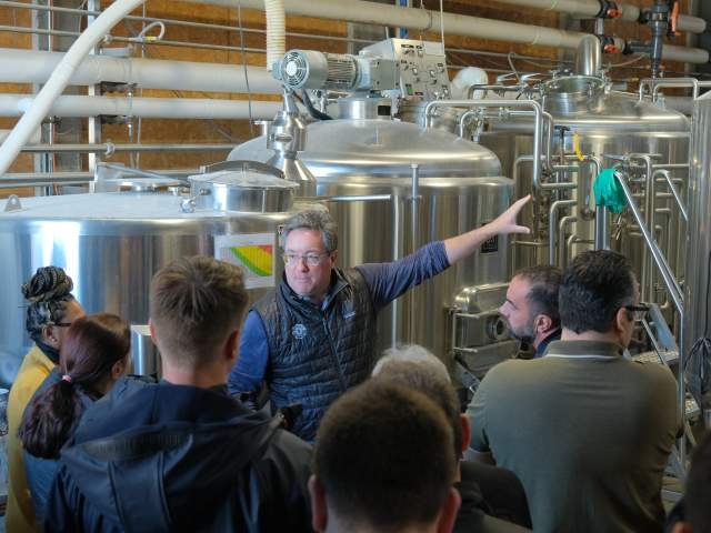 A group of people listening to a man speak inside a warehouse.