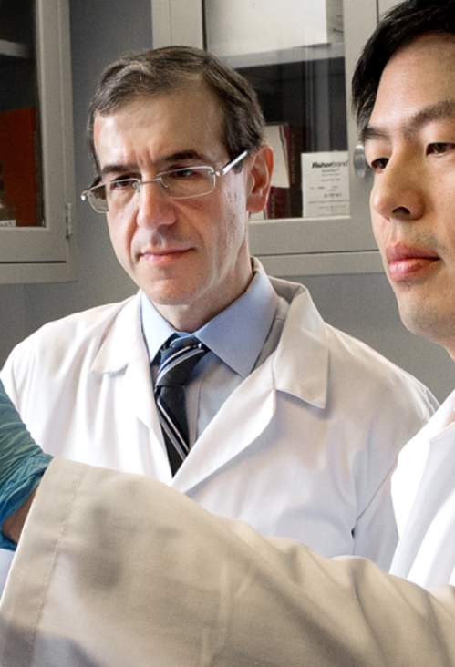 Two men in lab coats observing a petri dish inside a laboratory.